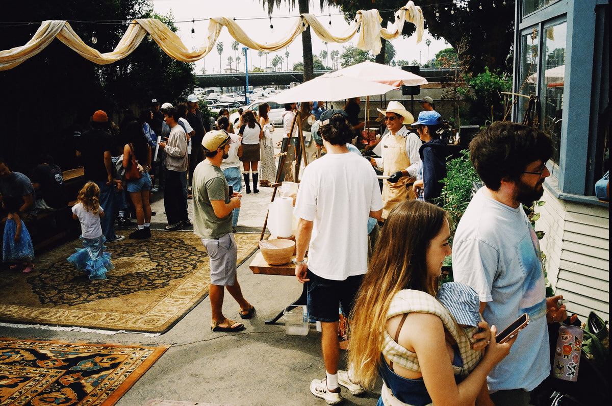 Crowd gathered under umbrellas and bunting at an outdoor Color Magic event